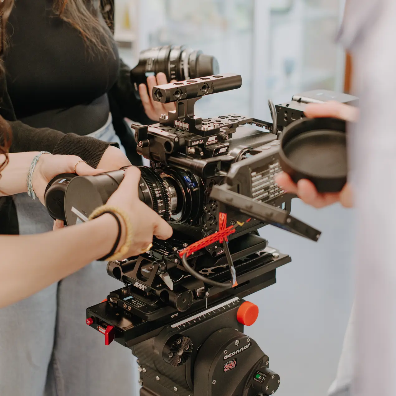 Eine Gruppe von Menschen arbeitet gemeinsam an einer Kamera. Eine Person hält eine Linse, während eine andere die Kamera justiert. Die Atmosphäre ist konzentriert und kreativ, symbolisiert das Filmemachen und Teamarbeit in einem modernen Umfeld.