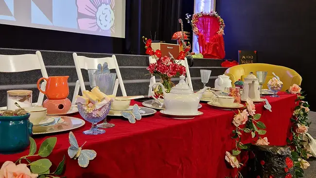 Auf der Bühne befindet sich ein reich mit Blumen, Teetassen und Schmetterlingen geschmückter Tisch