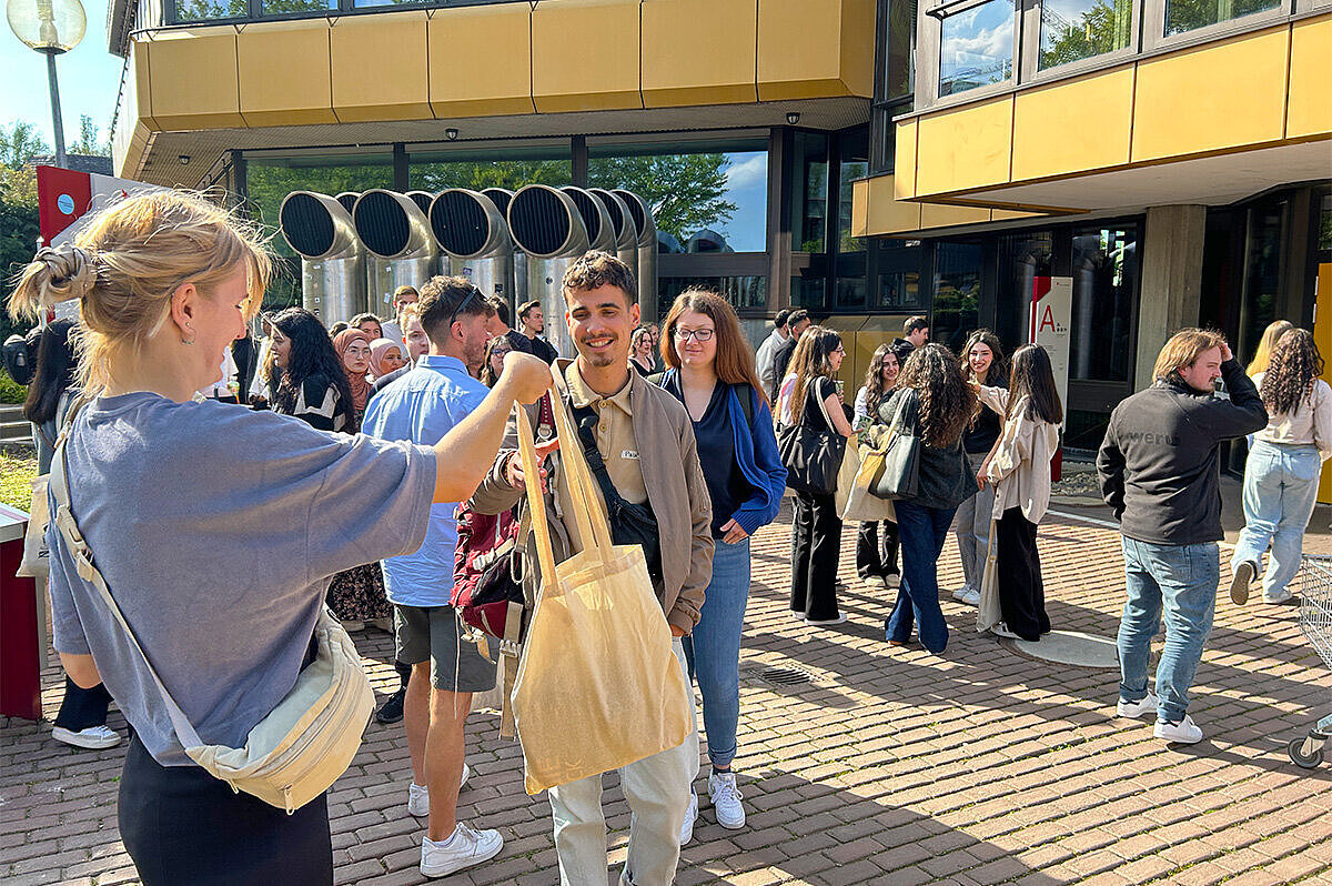 Vertreter:innen des AStA stehen auf dem Campus Kurt-Schumacher-Ring und verteilen die beliebten Ersti-Taschen.