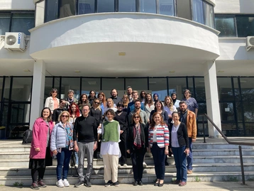 A group of about 40 people are standing on the steps of a modern building. They are participants in the UNESCO Chair workshop at RheinMain University of Applied Sciences. The diversity of the participants is evident as they smile and look at the camera. 