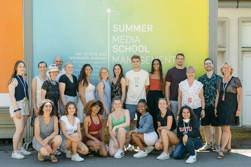 Gruppenfoto der Teilnehmer:inne der Media Mangement Summer School vor der Werbetafel auf dem Campus Unter den Eichen