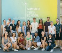 Gruppenfoto der Teilnehmer:inne der Media Mangement Summer School vor der Werbetafel auf dem Campus Unter den Eichen