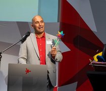 Hochschulkanzler Dr. Martin Lommel steht während seiner Abschiedsworte auf der Bühne und hält ein Windspiel in den Händen