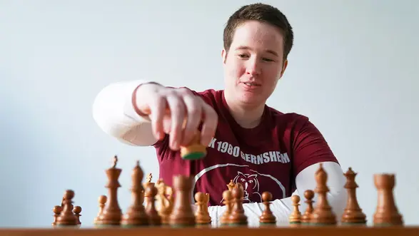 Porträt von Anne Lukas, Schach Anne Lukas vor einem Schachbrett sitzend, während sie zum nächsten Zug ansetzt.