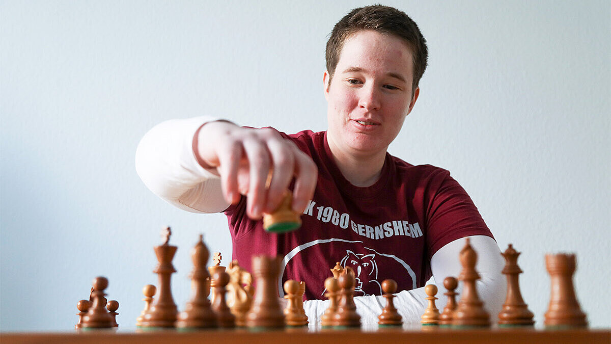 Porträt von Anne Lukas, Schach Anne Lukas vor einem Schachbrett sitzend, während sie zum nächsten Zug ansetzt.