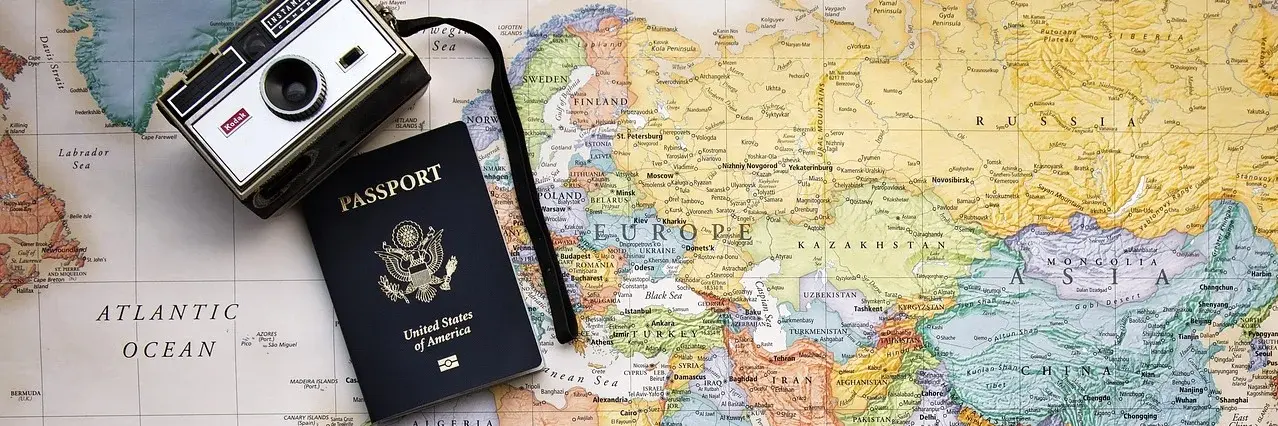 Auf dem Bild ist eine Weltkarte zu sehen,, auf der ein Reisepass sowie eine Kamera liegt