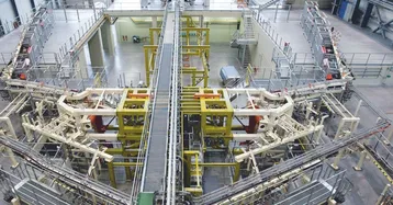 Eine hochmoderne Maschinenanlage in einem Industriegebäude. Im Zentrum befinden sich verschiedene mechanische Komponenten, die durch Förderbänder verbunden sind. Die Einrichtung scheint für Automatisierungs- oder Produktionsprozesse konzipiert zu sein, mit gesicherten Geländern und einem großen, offenen Raum im Hintergrund.
