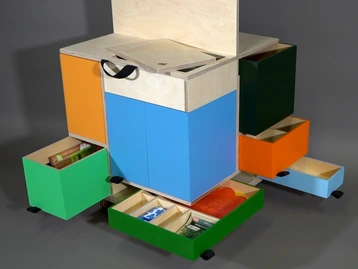 A modern storage unit with multiple colorful drawers in blue, green, orange, and red. The unit has an open top compartment with documents, and several drawers are partially pulled out, showcasing organized contents. The design emphasizes functionality and vibrant color coordination for easy access.