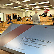 Ein Bildschirm auf dem eine Präsentationsfolie zu sehen ist mit der Überschrift "Künstliche Intelligenz im Finanzwesen. 10. Wiesbadener Versicherungskongress