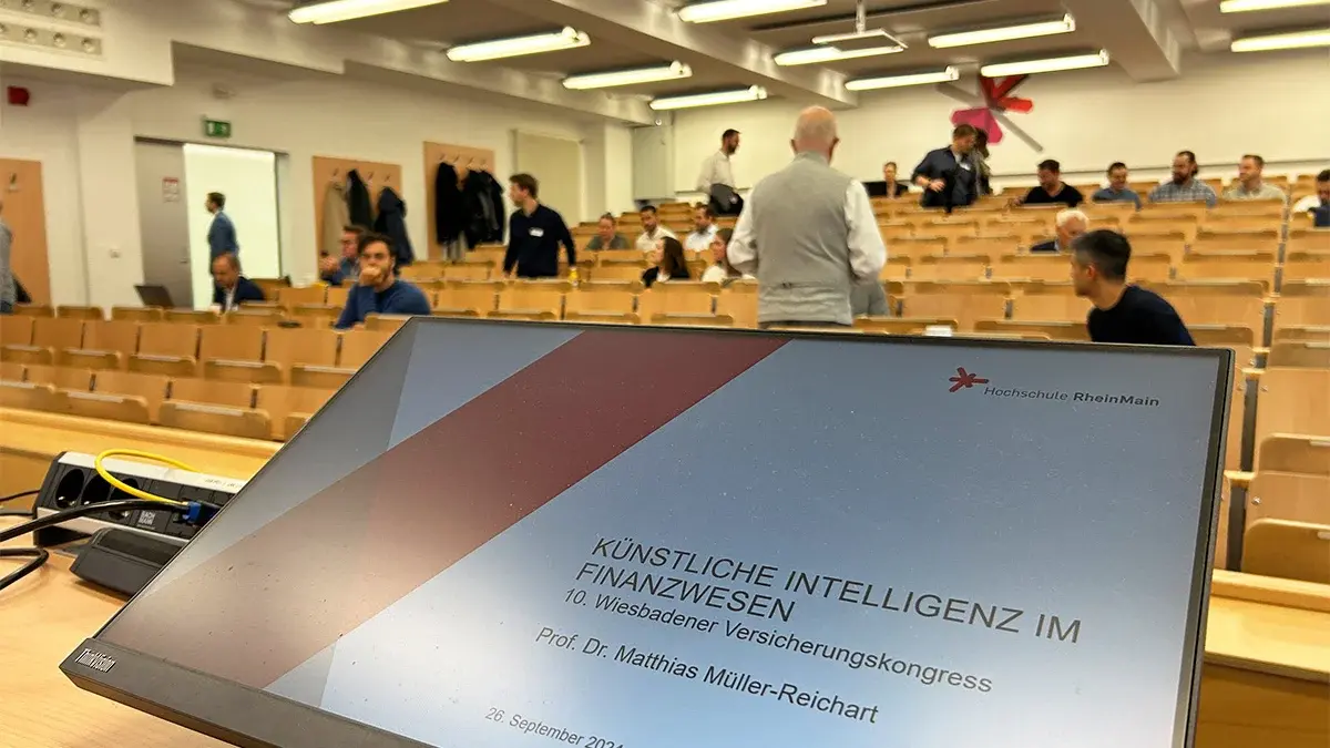 Ein Bildschirm auf dem eine Präsentationsfolie zu sehen ist mit der Überschrift "Künstliche Intelligenz im Finanzwesen. 10. Wiesbadener Versicherungskongress
