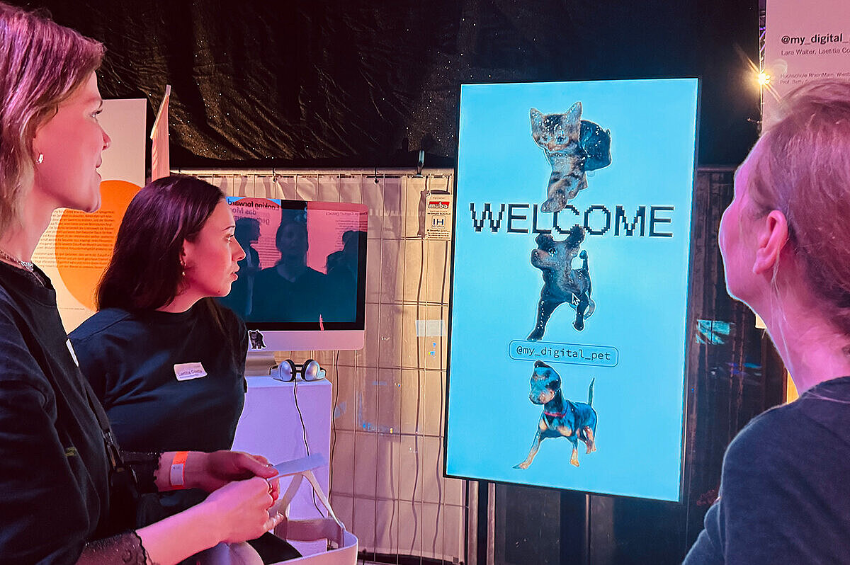 Drei Frauen schauen auf einen Screen, auf dem zwei Hunde und eine Katze und das Wort "Welcome" abgebildet sind