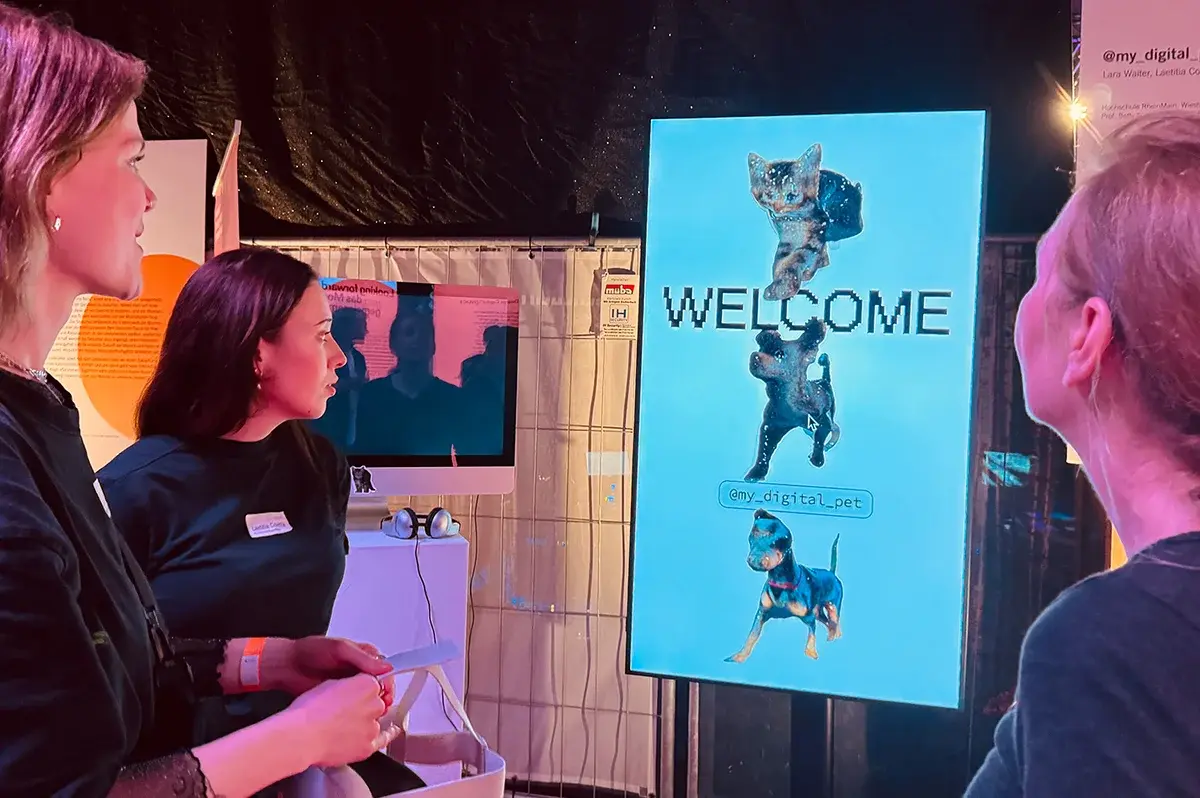 Drei Frauen schauen auf einen Screen, auf dem zwei Hunde und eine Katze und das Wort "Welcome" abgebildet sind