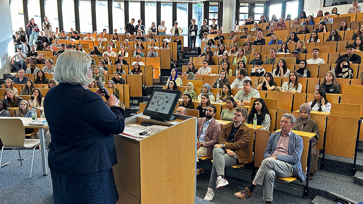 Hochschulpräsidentin Prof. Dr. Eva Waller steht am Rednerpult des Audimax und begrüßt die neuen Studierenden.