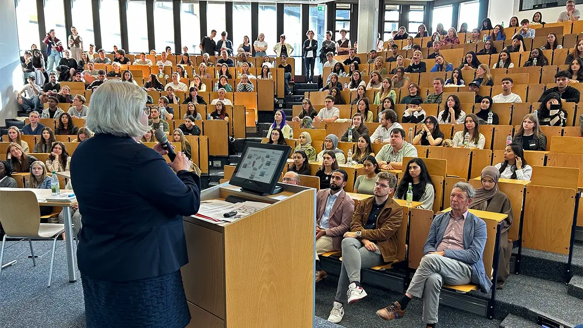 Hochschulpräsidentin Prof. Dr. Eva Waller steht am Rednerpult des Audimax und begrüßt die neuen Studierenden.