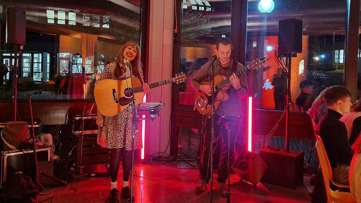 Melissa Muther und Nico Maas spielen Gitarre und singen für die Teilnehmer:innen des Studi-Dinners