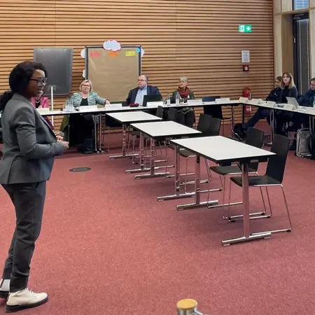 Präsentierende Professorin steht vor ihren Zuhörern, die an Tischen sitzen