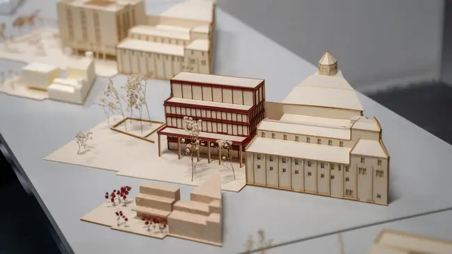 Modellansicht eines Gebäudekomplexes aus Holz mit einem auffälligen roten und transparenten Teil in der Mitte. Das Modell ist Teil einer Abschlussarbeit im Studiengang Architektur an der Hochschule RheinMain.