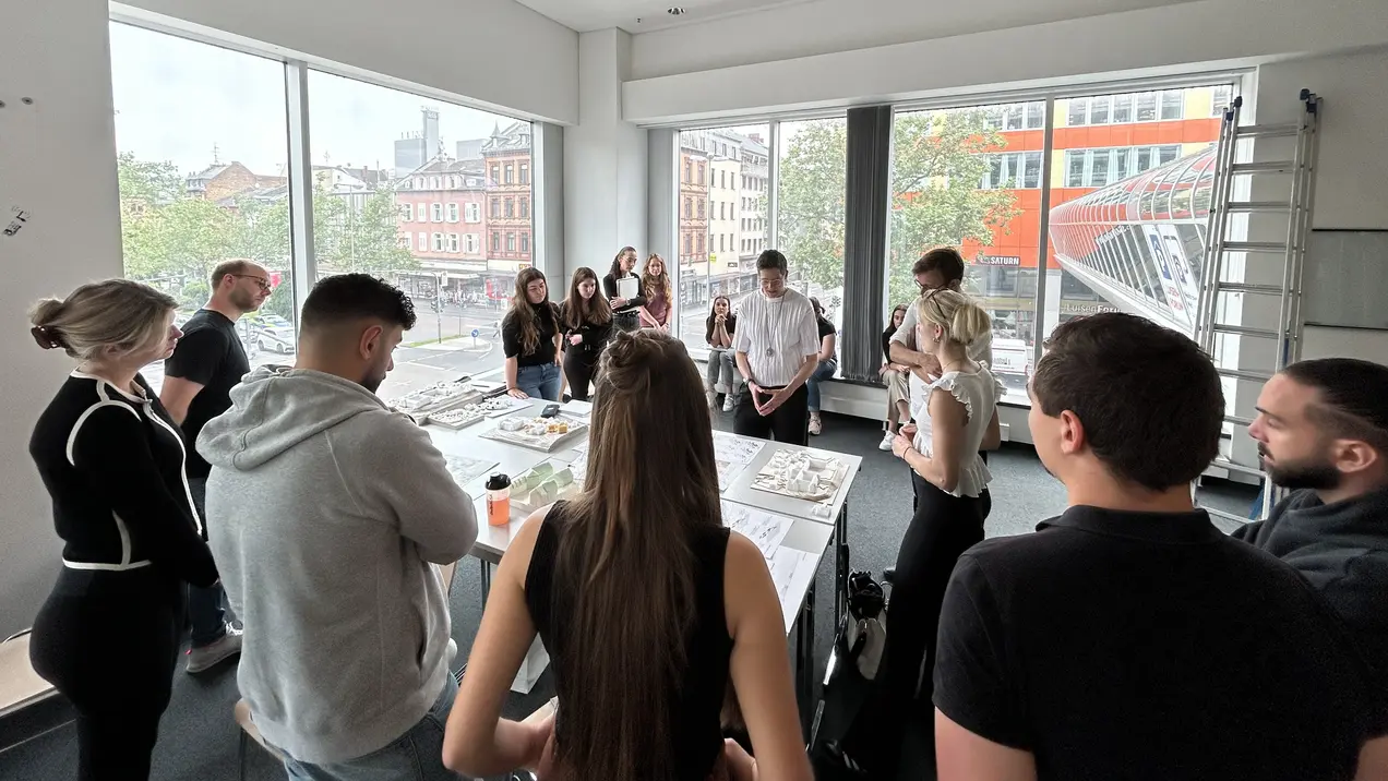 Architektur-Studierende stehen um Tische mit Modellen, im Hintergrund ist Wiesbadens Innenstadt zu sehen