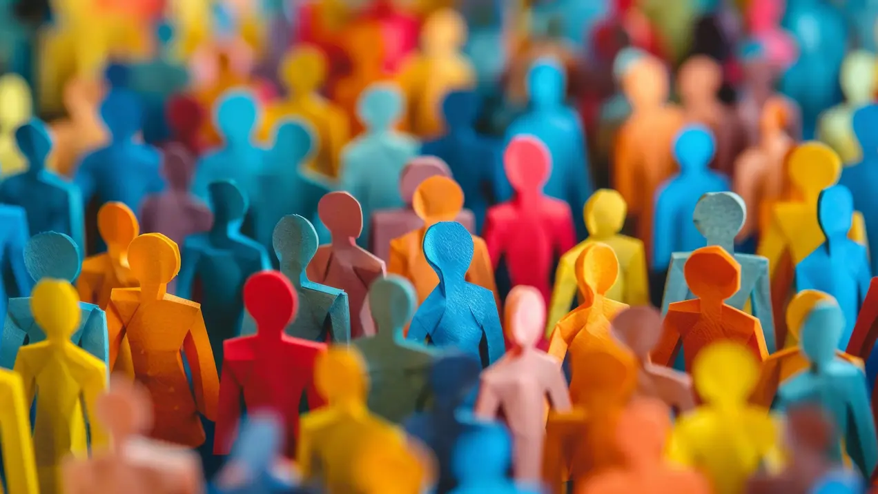 Ein dicht gedrängtes Feld aus bunten, stilisierten menschlichen Figuren in verschiedenen Farben. Die Figuren sind in zwei Dimensionen dargestellt und stehen in einem Muster, das Vielfalt symbolisiert. Die Szenerie vermittelt ein Gefühl von Gemeinschaft und Zusammenhalt.