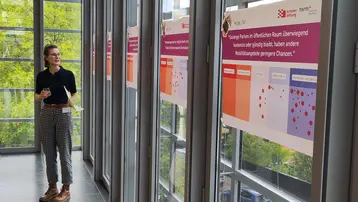 Eine Person steht in einem modernen Raum vor mehreren Informationsplakaten. Die Plakate thematisieren Barrierefreiheit im öffentlichen Raum und deren Einfluss auf Mobilität und Chancengleichheit. Es gibt Grafiken und Texte, die die unterschiedlichen Zugänglichkeiten veranschaulichen.