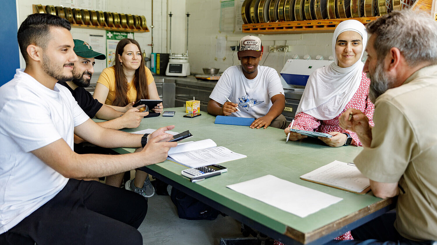 Studierende und Dozent sitzen gemeinsam am Tisch und beraten sich