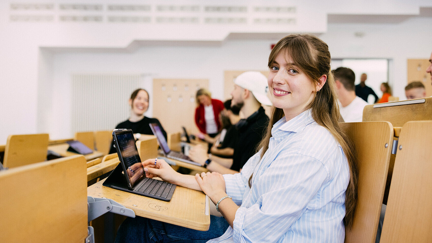 Studentin sitzt in einem großen Hörsaal mit aufgeklappten Tablet