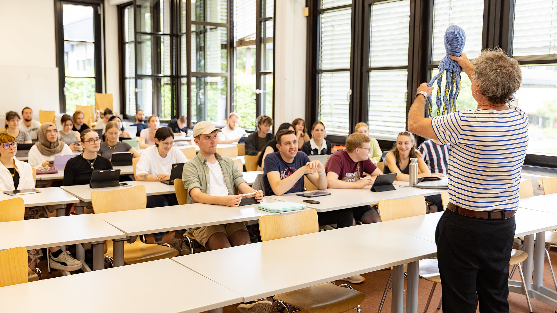 Seminar mit Studierenden und Lehrkraft Mann vor einer Gruppe junger Leute an Tischen