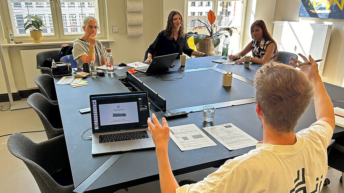 Vier Teilnehmer:innen des Innovation Camps 2024 sitzen an einem Tisch und arbeiten gemeinsam an ihrer Idee.