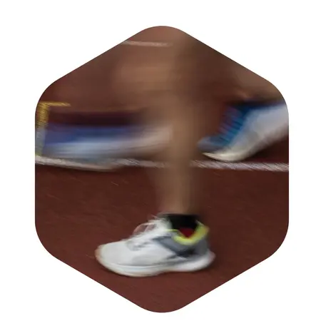 Eine verschwommene Nahaufnahme eines Laufenden Fußes in Sportschuhen auf einer Laufbahn. Die Bewegung vermittelt Dynamik und Geschwindigkeit.