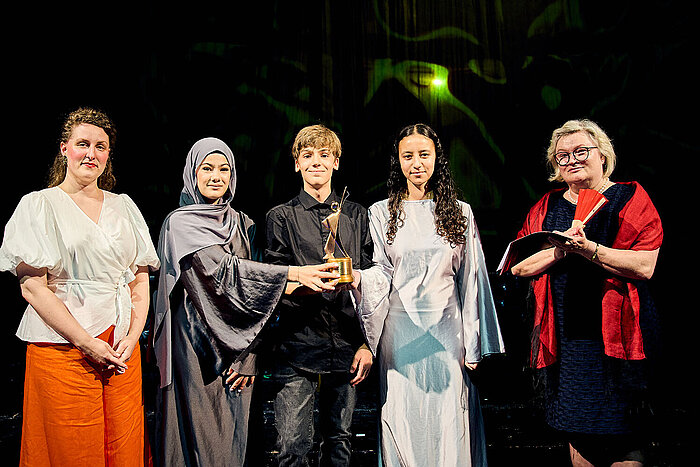 Prof. Dr. Eva Waller, Präsidentin der Hochschule RheinMain, steht mit Schüler:innen der Wilhelm-Heinrich-von-Riehl Schule auf der Bühne des Hessischen Staatstheaters.