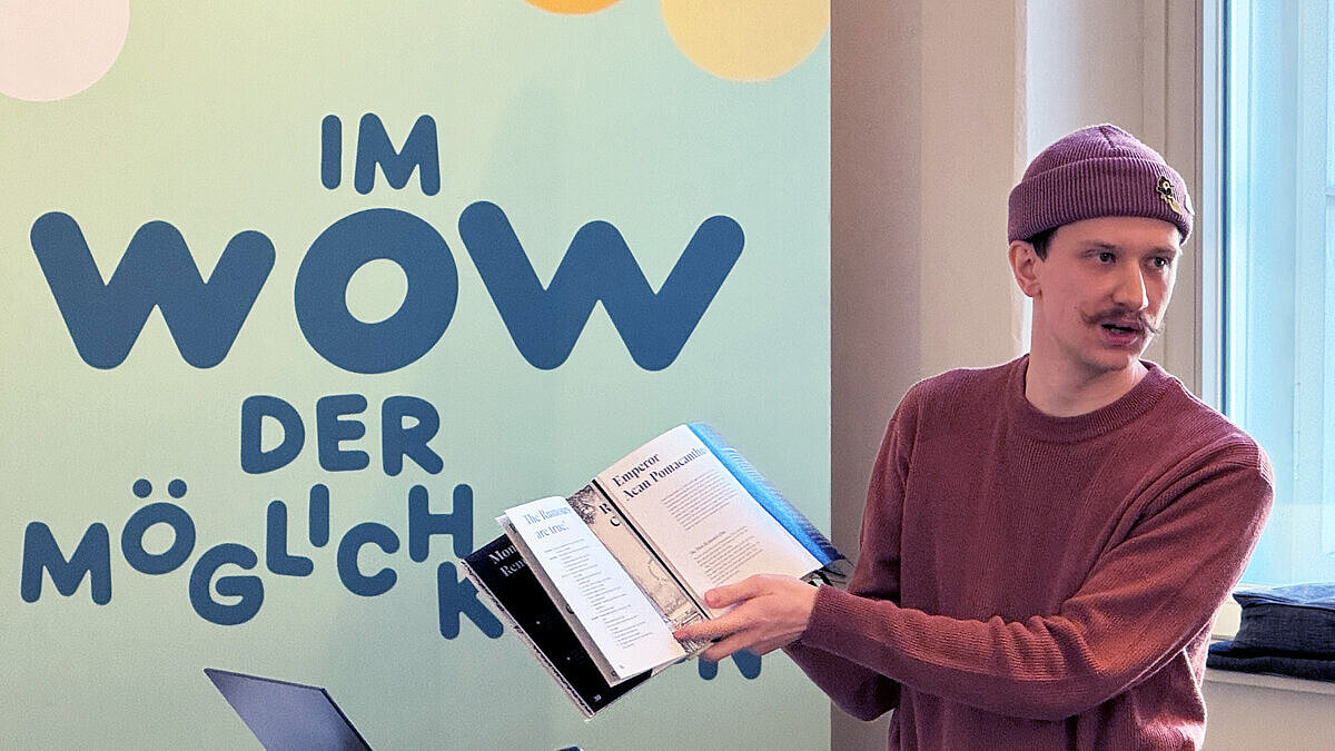 Ein junger Mann steht am Redepult und präsentiert eine Broschüre.