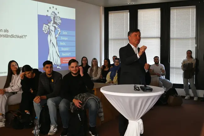 Prof. Bernd Wieberneit steht an einem Rednerpult und hält einen Vortrag. Im Hintergrund ist eine Präsentation mit dem Titel „Dein Europa: Bunt, spannend, realistisch?!“ zu sehen. Zahlreiche Zuhörer im Raum sind auf ihn konzentriert.