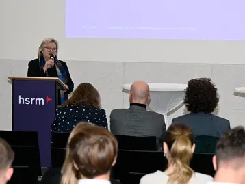 Präsidentin Prof. Dr. Eva Waller steht an einem Rednerpult der Hochschule RheinMain und spricht das Grußwort beim 2. Wiesbadener Tag für sozial nachhaltiges Investieren.