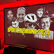 Blick auf die Leinwand mit einer Collage von Spitzensportler:innen der Hessischen Hochschule für öffentliches Management und Sicherheit und der Hochschule RheinMain, darüber der Text „Sportlerempfang 2024“
