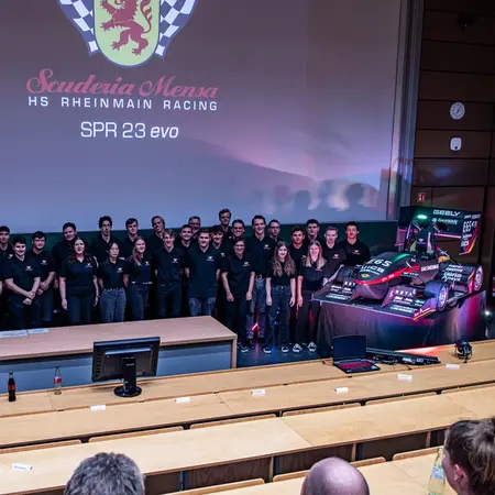 Studierende stehen auf der Bühne neben ihrem selbstgebauten Rennwagen