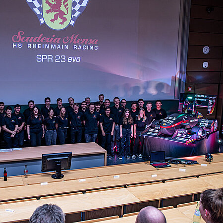 Vorstellung des neuen Rennwagens von Scuderia Mensa Studierende stehen auf der Bühne neben ihrem selbstgebauten Rennwagen