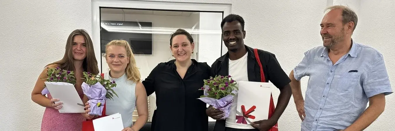 Personen stehen nebeneinander und lächeln in die Kamera. Sie halten Blumen und Zertifikate in ihren Händen 