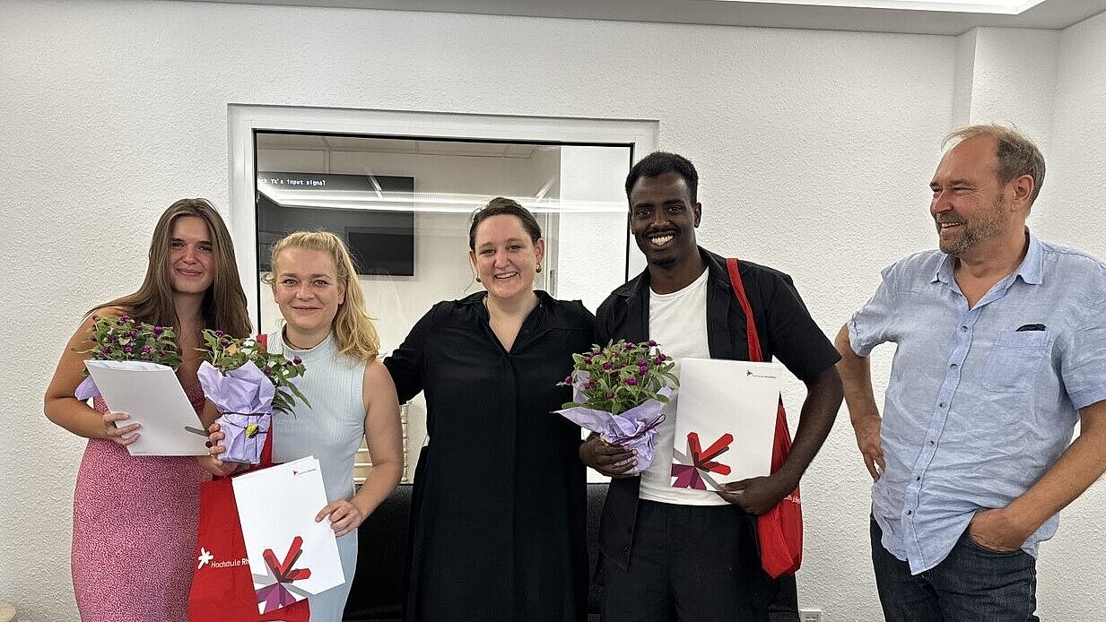 Personen stehen nebeneinander und lächeln in die Kamera. Sie halten Blumen und Zertifikate in ihren Händen 