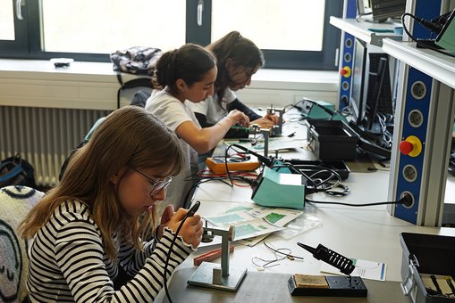 Drei Mädchen sitzen an einem Tisch und arbeiten mit Platinen und Lötkolben.