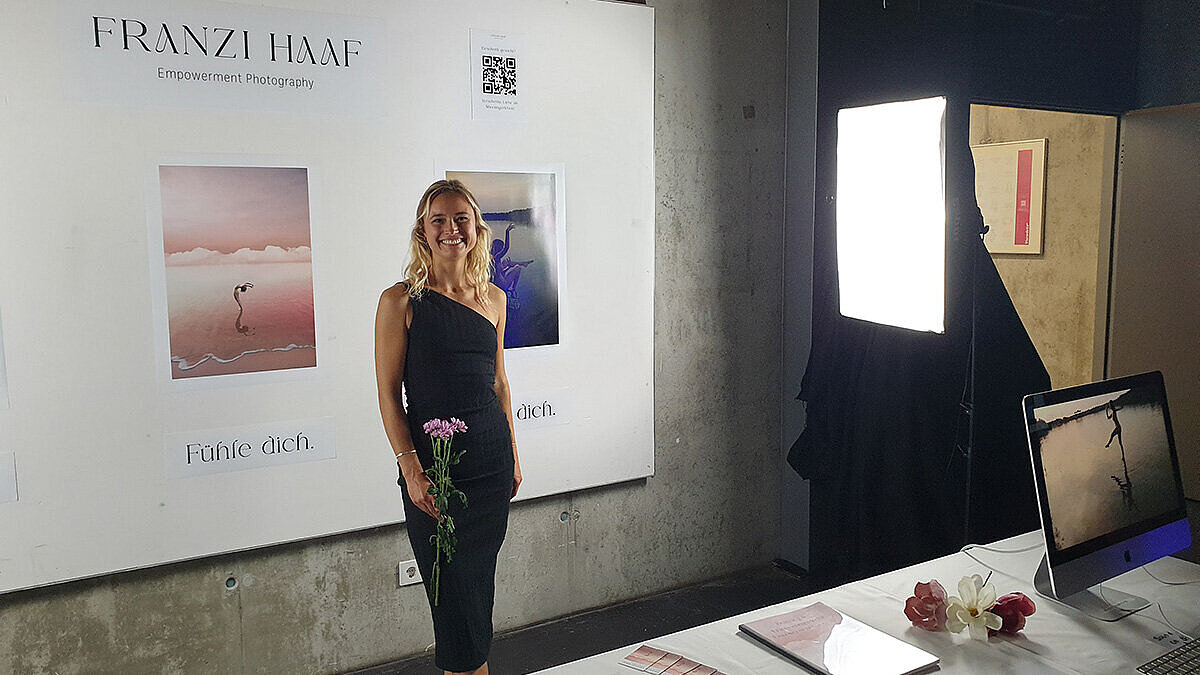 Absolventin Franziska Haaf steht vor einem Plakat mit ihren Fotografien