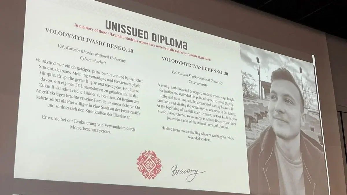 Auf einer Präsentationsfolie ist ein Diplom zu sehen mit einem Foto eines jungen Mannes, seinem Namen und Alters sowie einer kurzen Biografie. 