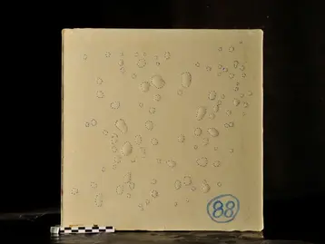 Ein quadratisches Stück Beton mit reaktionsharzgebundener Beschichtung. Darauf befinden sich Blasen, diese wurden umrandet als Markierung. Unten rechts steht in blau die Zahl „88“.