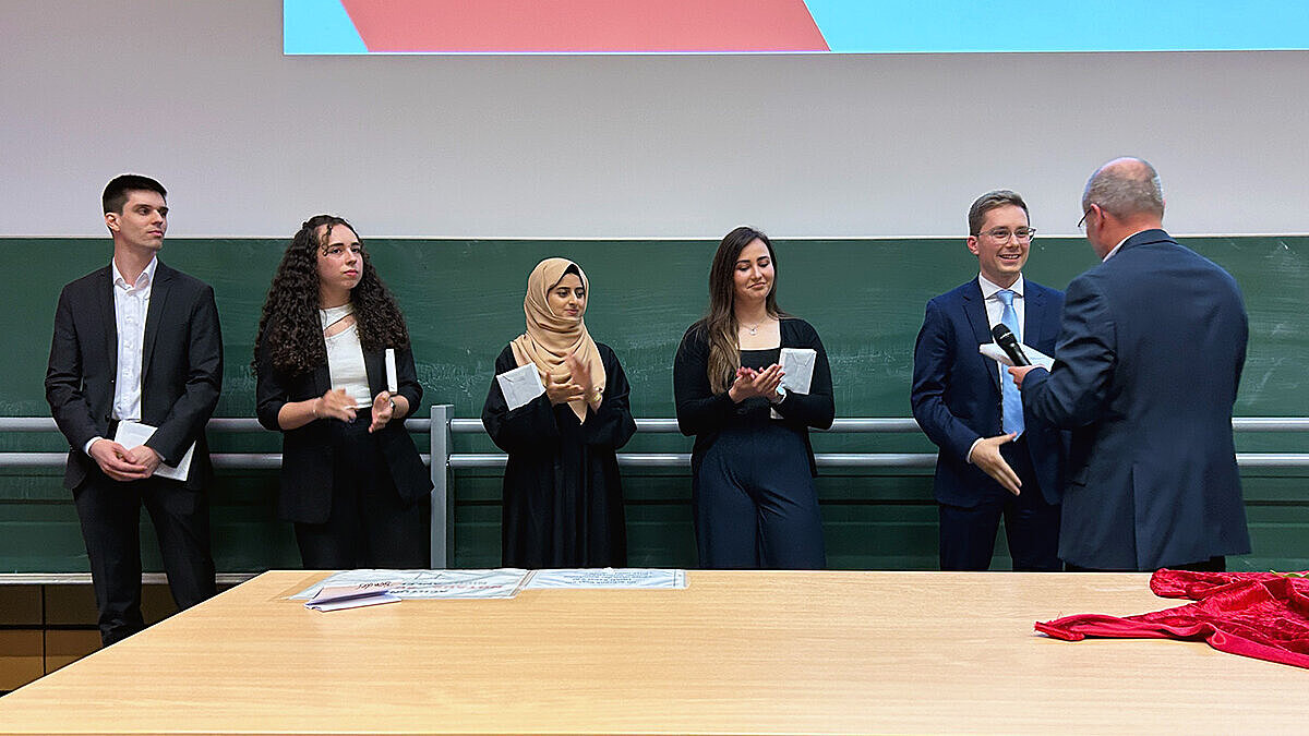 Fünf Absolvent:innen nehmen nacheinander die Glückwünsche eines Professors entgegen.
