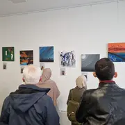 Besucher:innen betrachten die Bilder der Ausstellung, die vor einer weißen Wand hängen.