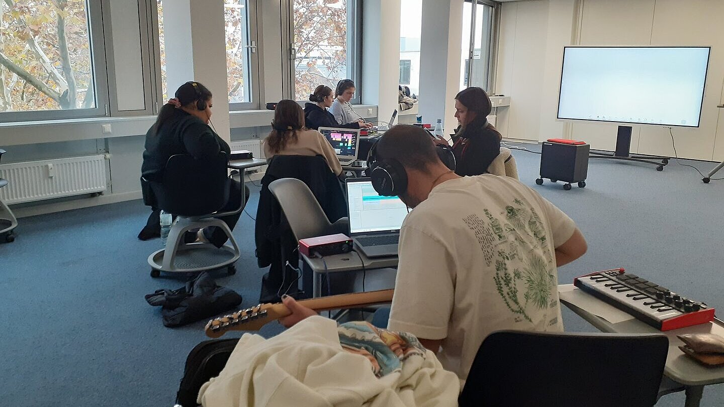 Junger Mann mit Kopfhörern auf den Ohren. Er hat eine Gitarre in der Hand 