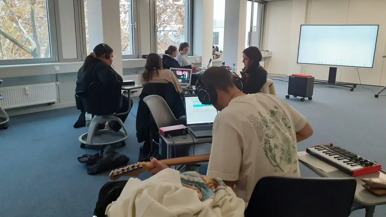 Junger Mann mit Kopfhörern auf den Ohren. Er hat eine Gitarre in der Hand 