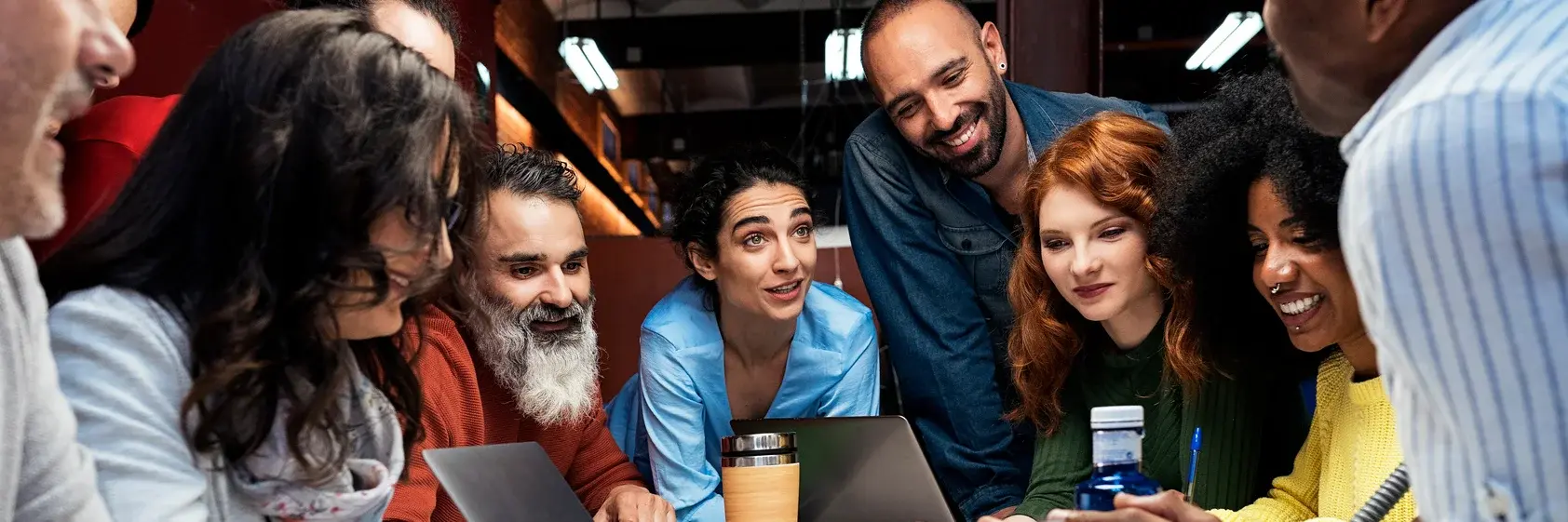 Eine Gruppe von Menschen um einen Tisch, die gemeinsam an einem Projekt arbeiten. Laptops und Notizen liegen vor ihnen. Alle scheinen engagiert und neugierig, während sie Ideen austauschen. Die Atmosphäre ist freundlich und kooperativ.