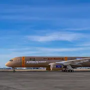 Ein Airbus A350 steht auf einem Flughafenrollfeld. Die Karosserie ist in einem sandfarbenen Design mit verschiedenen grafischen Elementen und dem Schriftzug „AIRBUS A350F“ verziert. Der Himmel ist klar und sonnig.
