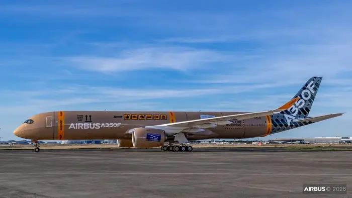Ein Airbus A350 steht auf einem Flughafenrollfeld. Die Karosserie ist in einem sandfarbenen Design mit verschiedenen grafischen Elementen und dem Schriftzug „AIRBUS A350F“ verziert. Der Himmel ist klar und sonnig.