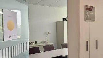 Ein Blick auf einen Büroraum durch eine Glastür. Der Raum enthält einen langen Tisch mit Stühlen und ist hell erleuchtet. Ein Informationsschild an der Tür zeigt die Raumnummer "B 6.1.80".